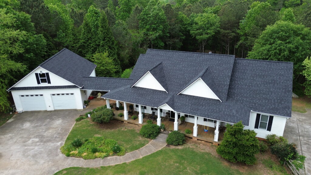 Aerial view of a white ranch home with a new charcoal architectural shingle roof and wraparound porch